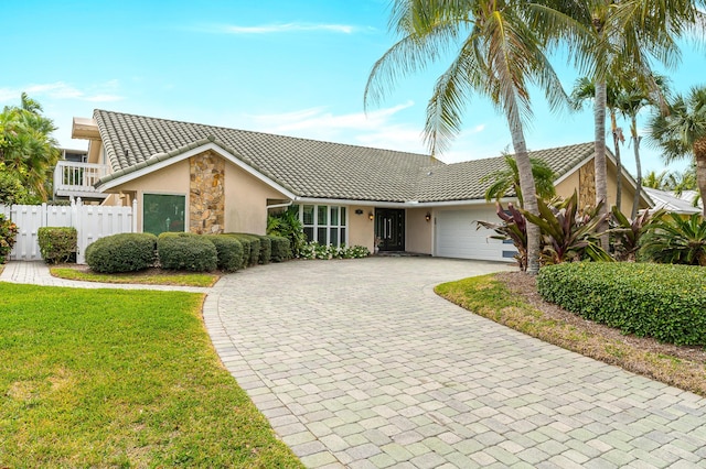 view of front of property with a garage, a tile roof, fence, stone siding, and decorative driveway