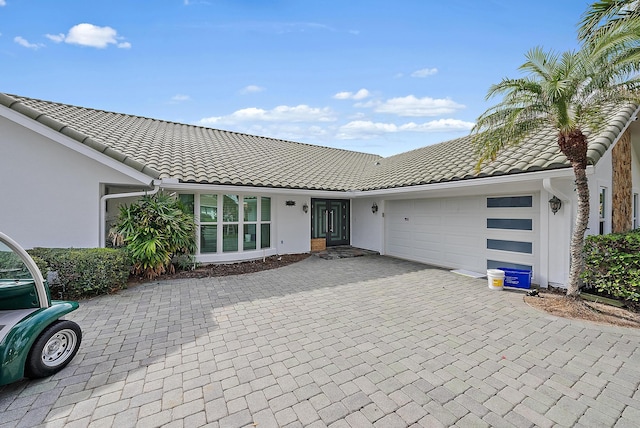 view of front facade with a garage, decorative driveway, a tile roof, and stucco siding