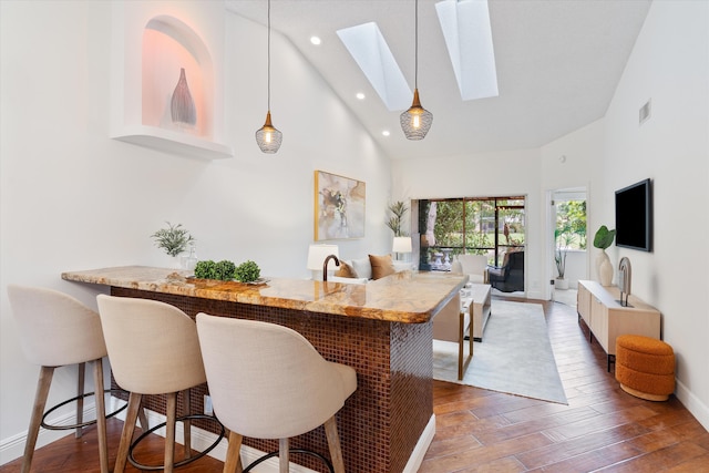 kitchen with high vaulted ceiling, a skylight, a breakfast bar area, and wood finished floors