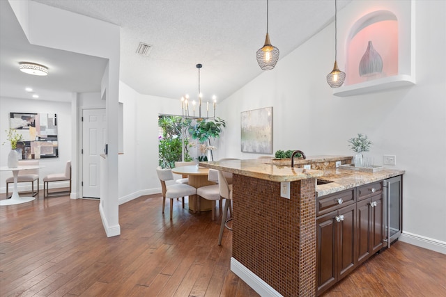 kitchen featuring lofted ceiling, dark wood-style flooring, a sink, visible vents, and dark brown cabinets