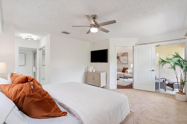 bedroom featuring a ceiling fan, light carpet, visible vents, and a textured ceiling