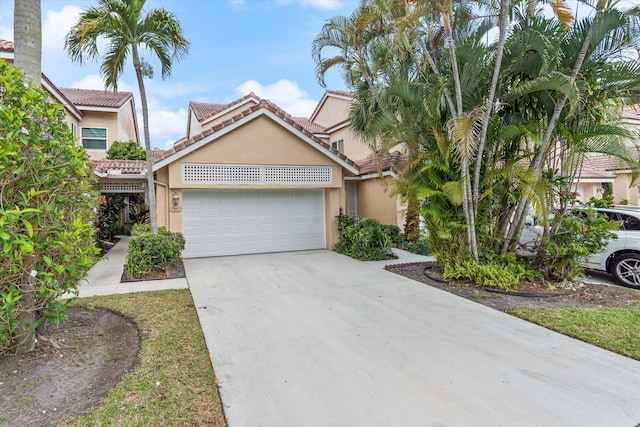 view of front of home featuring driveway, an attached garage, a tiled roof, and stucco siding