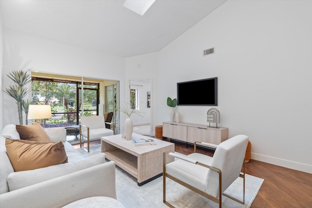 living area featuring a skylight, visible vents, wood finished floors, high vaulted ceiling, and baseboards