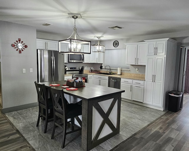 kitchen featuring stainless steel appliances, a sink, white cabinetry, light countertops, and decorative light fixtures