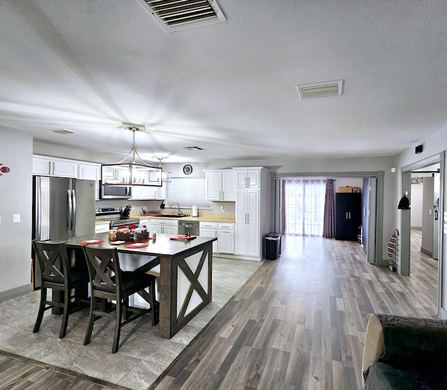 dining space with a chandelier, light wood-type flooring, visible vents, and a textured ceiling