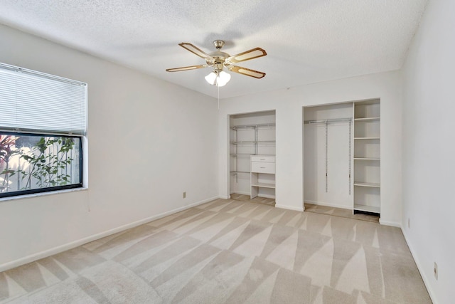 unfurnished bedroom featuring baseboards, multiple closets, a textured ceiling, and light carpet