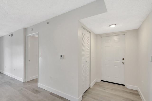 entrance foyer with light wood finished floors, baseboards, and a textured ceiling