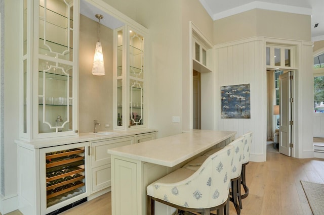 bar with bar area, hanging light fixtures, light wood-style floors, a sink, and beverage cooler