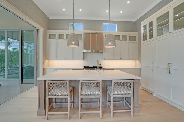 kitchen with light wood-style floors, light countertops, premium range hood, and a center island with sink