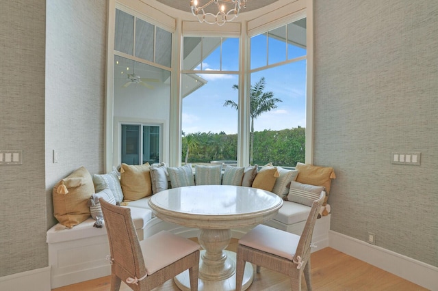 dining space with baseboards, ceiling fan with notable chandelier, wood finished floors, and wallpapered walls