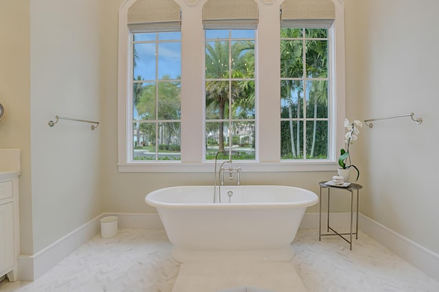 full bath with a freestanding bath, vanity, and baseboards