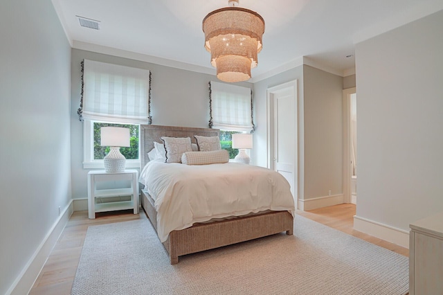 bedroom with a notable chandelier, crown molding, visible vents, light wood-style floors, and baseboards