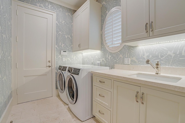 washroom featuring washing machine and clothes dryer, a sink, cabinet space, and wallpapered walls