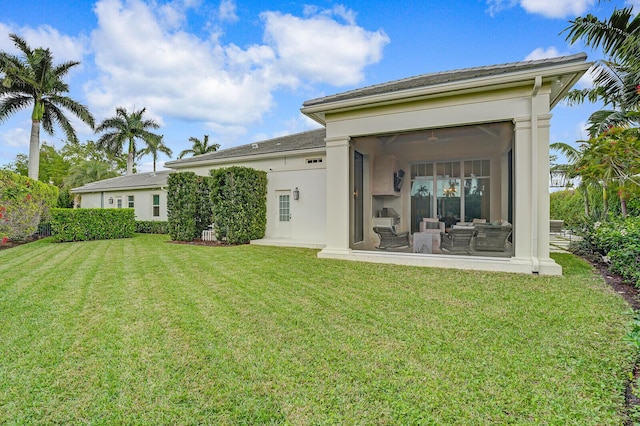 rear view of house featuring a sunroom, a lawn, and stucco siding