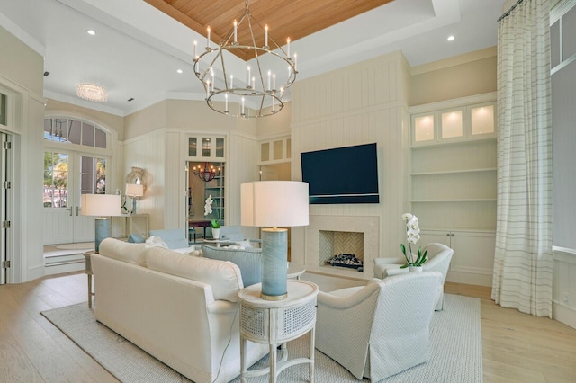 living area with a large fireplace, built in features, light wood finished floors, and an inviting chandelier