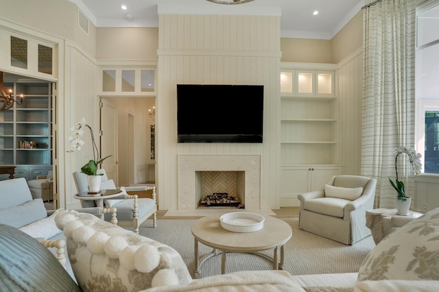 living area with a fireplace, built in features, a notable chandelier, and ornamental molding