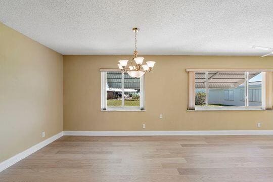 spare room featuring a chandelier, baseboards, a textured ceiling, and wood finished floors