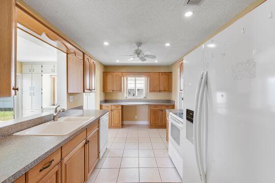 kitchen featuring a ceiling fan, a sink, a textured ceiling, white appliances, and light tile patterned flooring