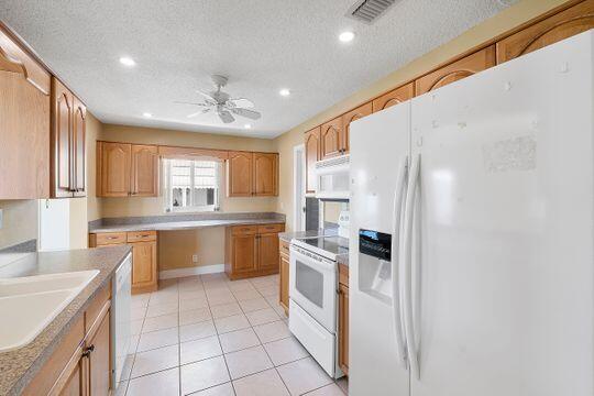 kitchen with a sink, white appliances, a textured ceiling, and a ceiling fan