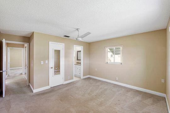 unfurnished bedroom with visible vents, a textured ceiling, connected bathroom, carpet, and baseboards