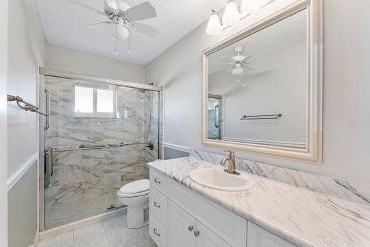 full bathroom featuring a marble finish shower, toilet, vanity, and ceiling fan