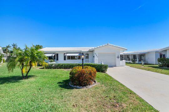 ranch-style house with stucco siding, driveway, an attached garage, and a front lawn