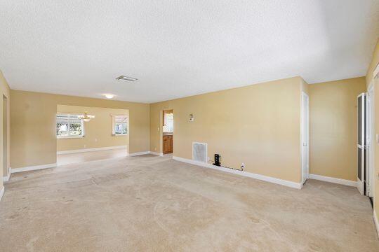 spare room with light carpet, visible vents, baseboards, and a textured ceiling