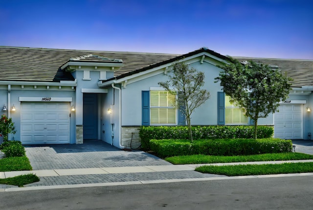 view of front facade featuring a garage, decorative driveway, a tile roof, and stucco siding