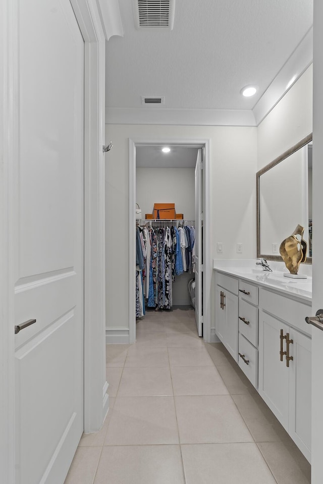 bathroom featuring vanity, visible vents, a spacious closet, ornamental molding, and tile patterned floors