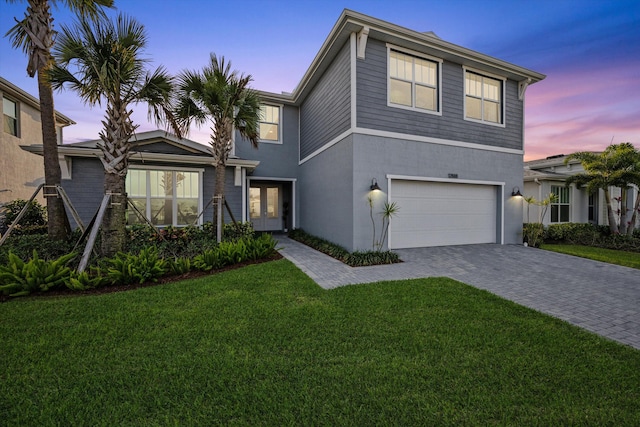 view of front facade with a garage, a yard, decorative driveway, and stucco siding