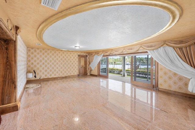 unfurnished living room with baseboards, granite finish floor, visible vents, and wallpapered walls