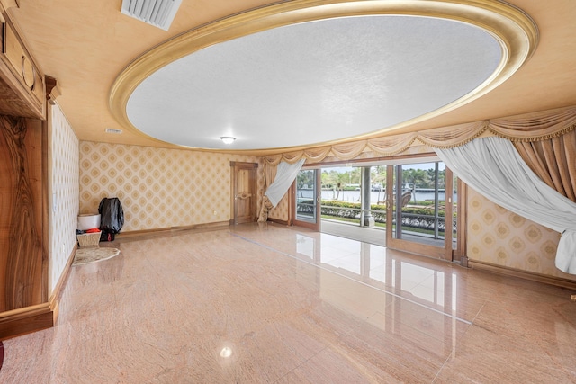 unfurnished living room with wallpapered walls, visible vents, granite finish floor, and baseboards