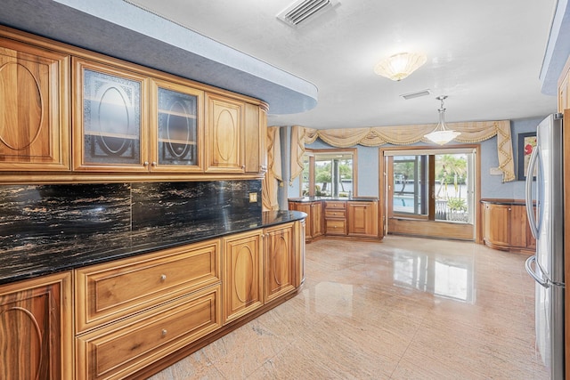 kitchen with brown cabinetry, freestanding refrigerator, visible vents, and glass insert cabinets