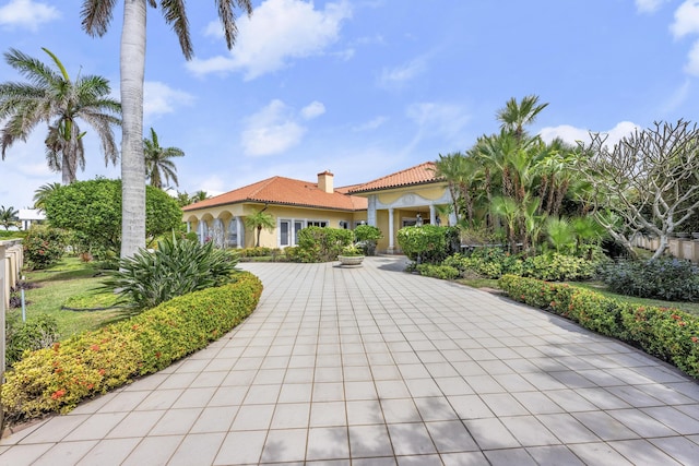 mediterranean / spanish-style house featuring a tile roof, a chimney, and stucco siding