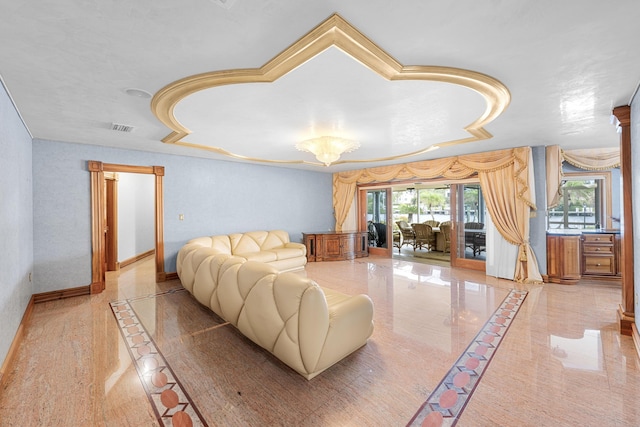 living area featuring ornate columns, baseboards, visible vents, and a tray ceiling