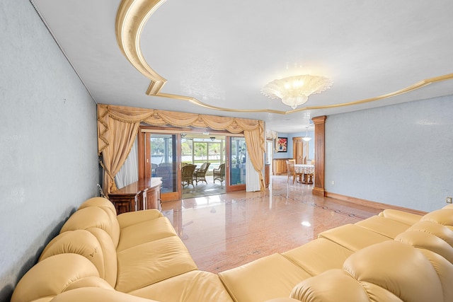 living area with a textured wall, a raised ceiling, a notable chandelier, and baseboards