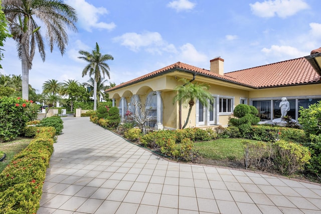 view of side of home featuring a tiled roof, a chimney, and stucco siding