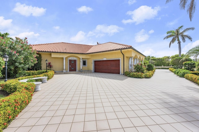 mediterranean / spanish-style house with a garage, decorative driveway, a tile roof, and stucco siding