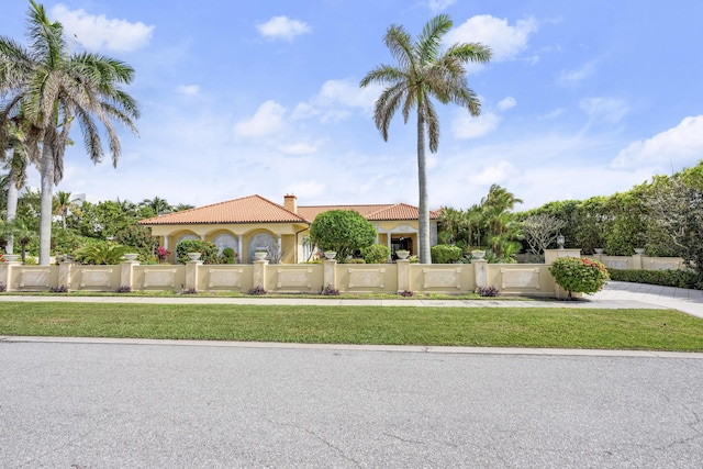 mediterranean / spanish home featuring a fenced front yard, a tile roof, a chimney, and stucco siding