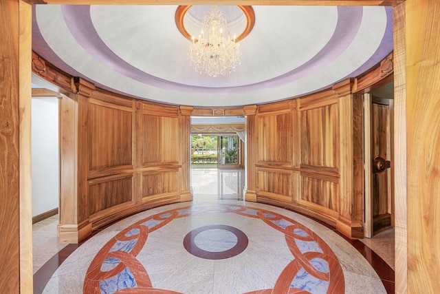 interior space with a tray ceiling, an inviting chandelier, wood walls, access to outside, and baseboards