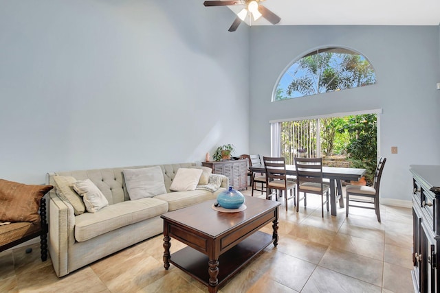 living room featuring light tile patterned flooring, baseboards, a ceiling fan, and a towering ceiling