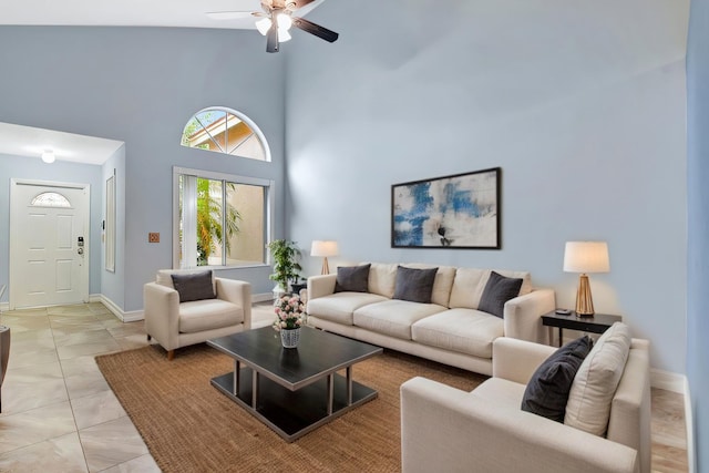 living room featuring light tile patterned floors, baseboards, ceiling fan, and a towering ceiling