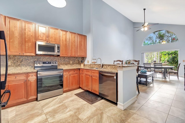 kitchen featuring a ceiling fan, a sink, stainless steel appliances, a peninsula, and light stone countertops