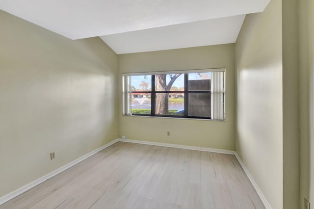 spare room featuring vaulted ceiling, light wood-style flooring, and baseboards