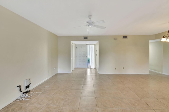 empty room with visible vents, ceiling fan with notable chandelier, baseboards, and light tile patterned flooring