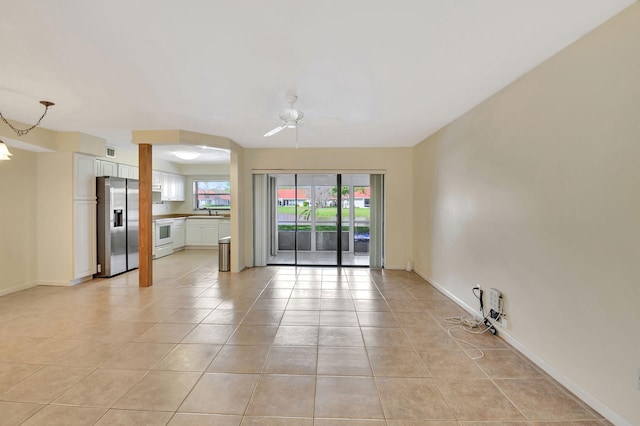 empty room featuring a ceiling fan, light tile patterned flooring, a sink, and baseboards