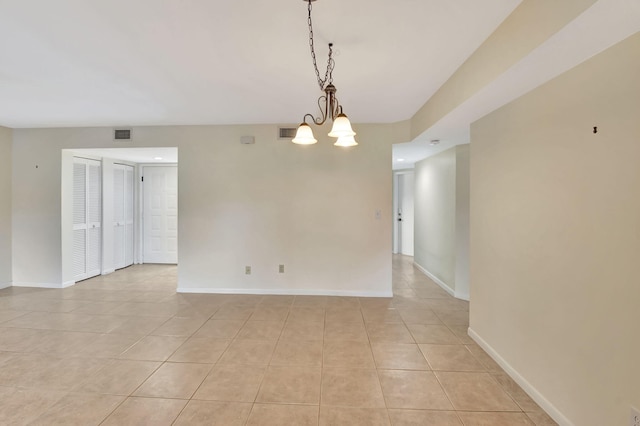 empty room featuring light tile patterned floors, baseboards, visible vents, and a notable chandelier