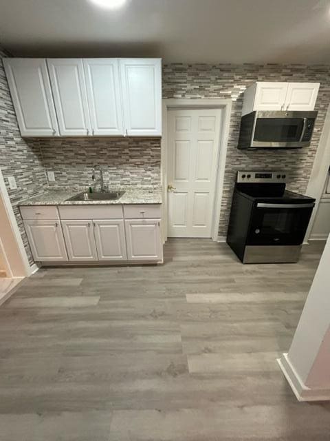 kitchen featuring appliances with stainless steel finishes, a sink, light wood-style floors, and white cabinets