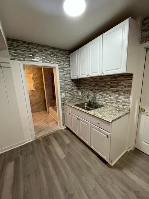 kitchen with decorative backsplash, white cabinets, a sink, and wood finished floors