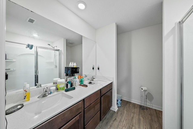 bathroom featuring double vanity, wood finished floors, a sink, and a shower stall